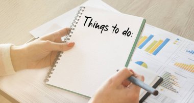 Ofisteki bir masada oturan bir iş kadını not defterine bakar. Planlar, hedefler, planlar. Yakın çekim, yumuşak ışık.