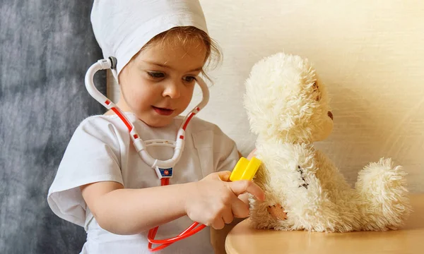 Şirin küçük kız doktorculuk oynuyor. Beyaz üniforma giymiş sevimli bir çocuk termometre ve stetoskop tutuyor..