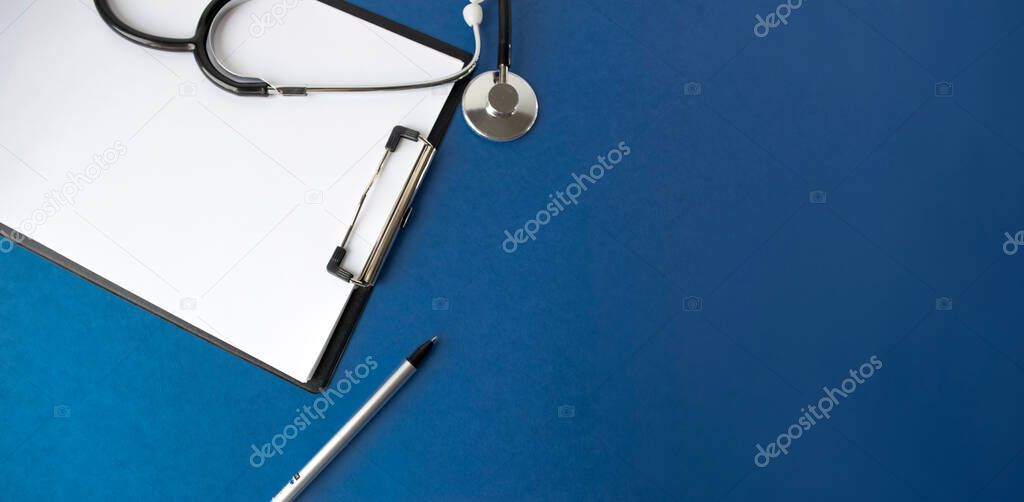 Medical stethoscope and clipboard with a blank sheet of paper on a blue background. View from above. Medical concept.