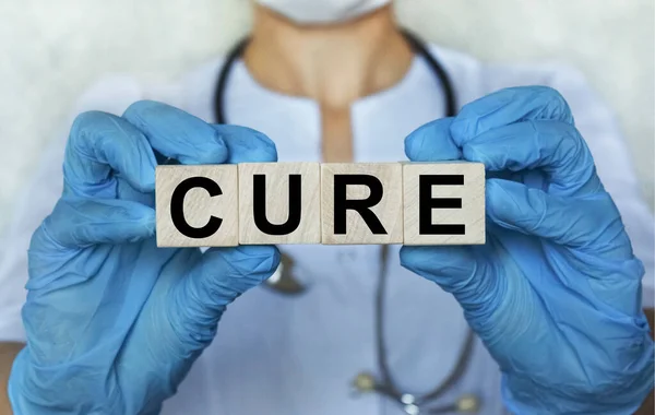 word CURE on wooden cube blocks in the hands in protective gloves of a doctor woman. Blurring doctor on background