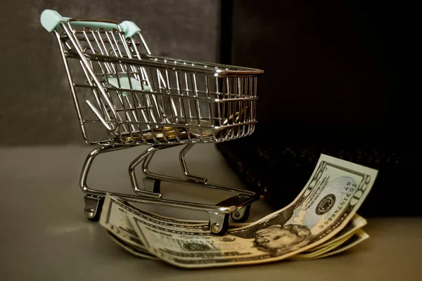 Toy little cart with money near the laptop on a dark background, along with money bills. Business and financial concept.