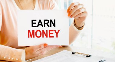 Elinde tabela olan açık renk elbiseli bir kız masada oturuyor. - Para biriktiriyorum. İçerik harfleri iş kavramına karşılık gelir.