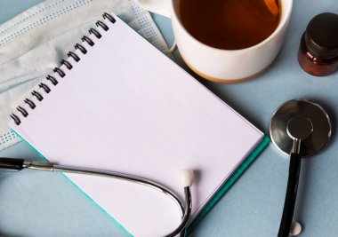 Doktor 'un masası ofiste. Yukarıdan bak. Bir stetoskop, defterde boş bir sayfa kağıt, tıbbi maske ve bir fincan çay. Tıbbi konsept.