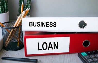 Masaüstünde hesap makinesi ve kalemle birlikte duran kırmızı ve beyaz klasörler. Dosyadaki harflerin finansal ya da pazarlama önemi var. İş konsepti.