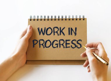 White paper with the text WORK IN PROGRESS in female hands on a white background. Close-up, soft light. Marketing concept.