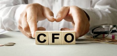 Ahşap küplerin dokusunda CFO yazıları var. Bir iş adamı elinde bir küp tutuyor. Finansal, ticari ya da ekonomik tema üzerine bir yazı.