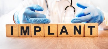 Mavi eldivenli genç bir erkek doktor IMPLANT yazılı küpleri tutuyor. Sağlık ve Tıp Konsepti.