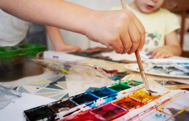 Çocuğa yakın el fırçası tutuyor. Çocuk resimlerle bir resim çiziyor..