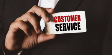 Beyaz gömlekli ve siyah takım elbiseli siyah bir adam kameraya bir kartvizit gösteriyor. Harflerin içeriğinin iş konsepti ve pazarlama üzerinde etkileri vardır..