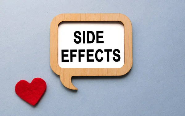The inscription SIDE EFFECTS on a wooden template, against the background of scattered a red heart. Medical concept.