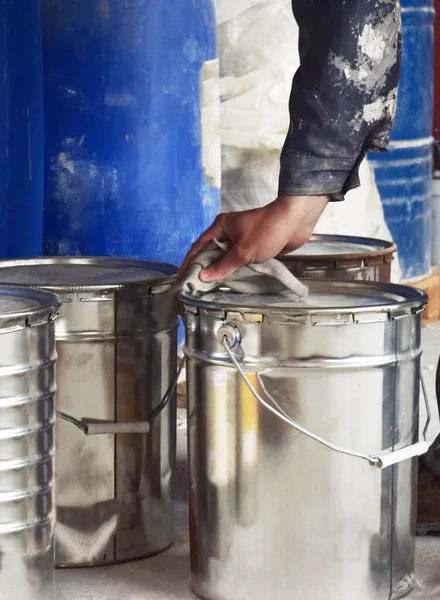Production of paints. A worker in a suit with traces of paint stands near a paint can. Storage room for paints.