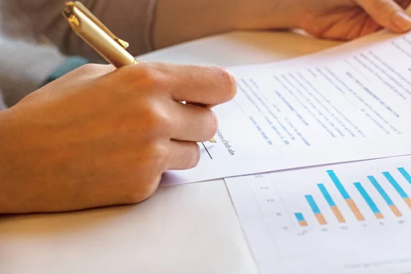 Young business woman signs a business contract on the background of economic charts while sitting at the table. Business and finance concept. Selective focus.