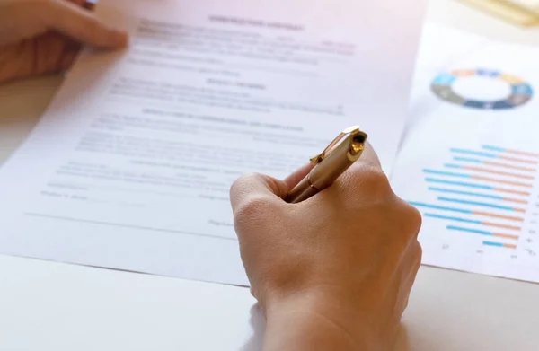 Young business woman signs a business contract on the background of economic charts while sitting at the table. Business and finance concept. Selective focus.