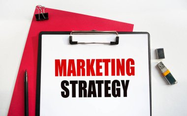 MarkeTing STRATEGY etiketli bir klipsli klasör. İş aksesuarlarıyla birlikte çalışma masasının üst görüntüsü. Finans ya da iş konsepti.