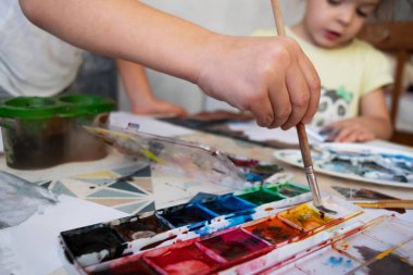 Çocuğa yakın el fırçası tutuyor. Çocuk resimlerle bir resim çiziyor..