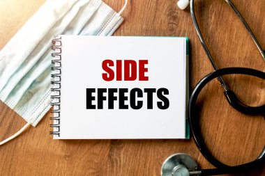 Yazı - Yan Etkinlik (yan etki). Neyin önemli olduğunu hatırlatmak için bir not defterine yazılmış. Masanın üst görüntüsü steteskop ve maskeyle birlikte. Sağlık hizmeti kavramı.