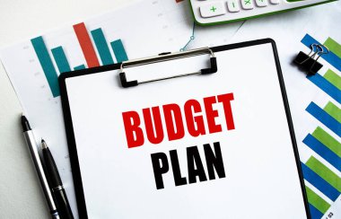 Bütçe Planı etiketli bir klipsli klasör. Belgeler, çizelgeler ve iş aksesuarlarıyla birlikte bir masaüstü görüntüsü. Finans ya da iş konsepti.