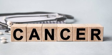 CANCER inscription on wooden cubes isolated on white background, medicine concept. Nearby on the table are a stethoscope and pills.