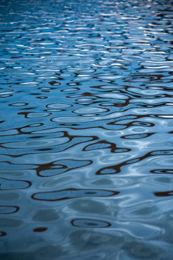 Suyun mavi yüzeyinde desenler ve dalgalanmalar var. Dalgalarda güzel bir güneş parlıyor. Doğal arkaplan dokusu.