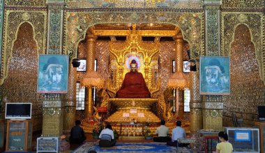 Tayland tapınağındaki altın Buda heykelinin yakınındaki insanlar