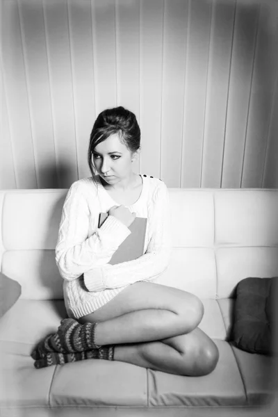 Woman in sweater holding a book on sofa — Stock Photo, Image