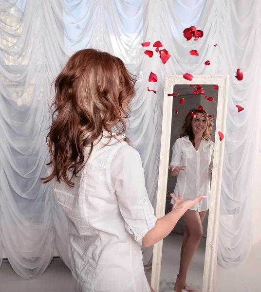 Donna gettando petali di rosa vicino allo specchio — Foto Stock