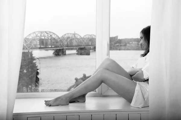 Doordachte vrouw met een boek zitten in de buurt van venster — Stockfoto