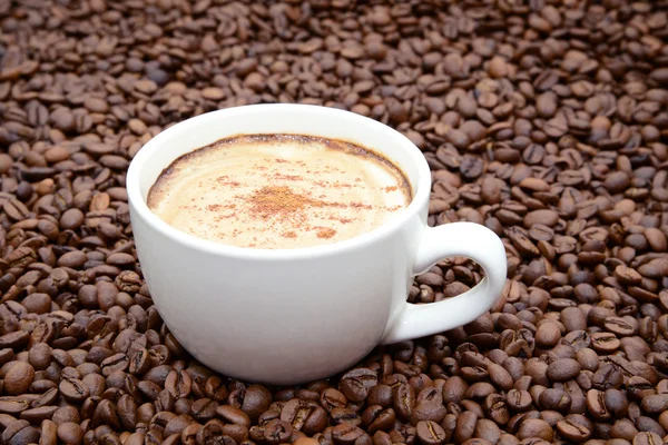 Cup of coffee with cinnamon on a coffee beans background — Stock Photo, Image