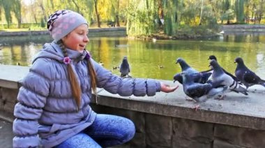 Oturan kız güvercinleri elinden beslenir.