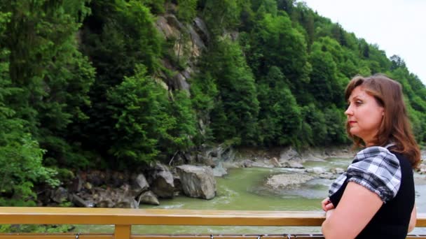 Mujer en puente entonces mira en cascada — Vídeo de stock