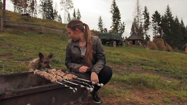 Девушка сидит рядом с Мангалом с собакой — стоковое видео