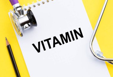 Vitamin - steteskop ve sarı arka planda kalemle deftere yazılmış metin