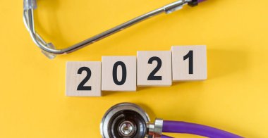 2021 numaralı tahta küpler ve sarı arka planda steteskop. Tıbbi beklenti 2021 konsepti.