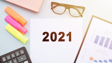 2021 metni, hesap makinesi, keçeli kalemler, gözlükler ve finansal tablolarla birlikte bir ofis masasının üzerinde beyaz kağıda yazılmıştır. İş konsepti.
