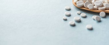 Beyaz haplar, mavi masadaki tahta kaşıkta tabletler. Tıp ve sağlık konsepti. Eczacılık. Haplar ve vitaminler.