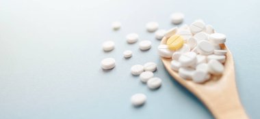 Beyaz tabletler ve mavi arka planda ahşap kaşıkta bir sarı tablet.