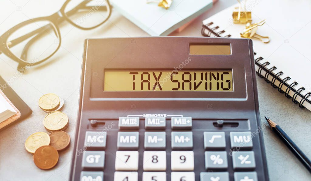 Calculator with text Tax Saving. Calculator, glasses, book, money and pen on table. Business, finance conceptual.