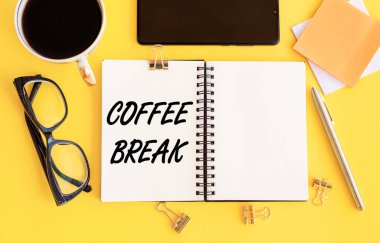 Sarı bir masanın üzerine deftere ve kırtasiyeye yazılmış kahve molası metni..