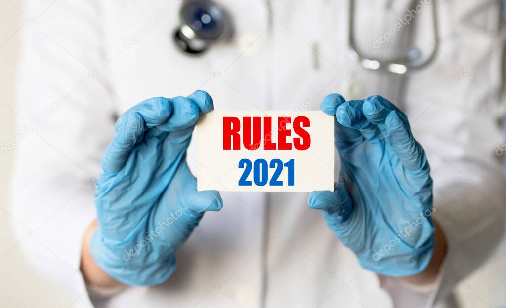 A medical worker in gloves holds a card with the words RULES 2021. Concept of rules in medicine for 2021