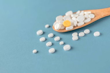 Ahşap kaşıkta haplar açık mavi arka plan çapraz işleminde. Tıbbi konsept