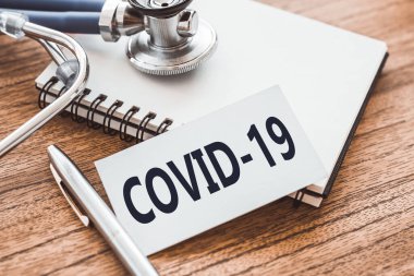 Tahta masada, üzerinde steteskop ve tıbbi not defteri olan COVID-19 metni. Coronavirus, tıbbi konsept.