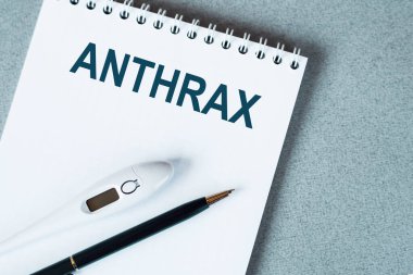 Masanın üzerinde termometre ve kalem olan boş bir defter. ANTHRAX kelimesi.