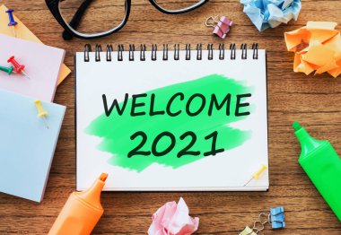Not defteri olan ahşap masa. Kalemler, ataçlar ve buruşuk kağıtlarla 2021 'e hoş geldin. İş konsepti üst görünümü.
