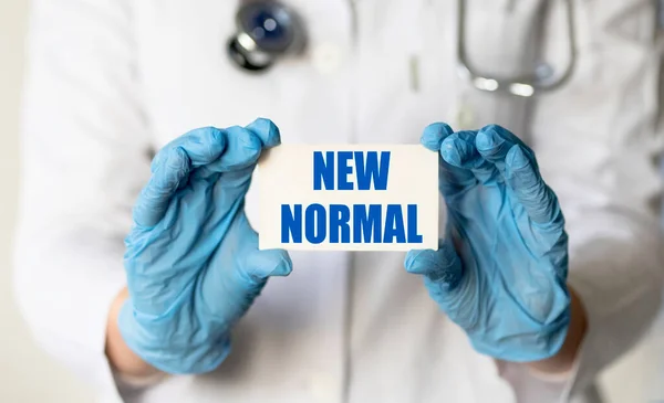 A medical worker in gloves holds a card with the words NEW NORMAL. Medical concept. Covid 19 and coronavirus concept.