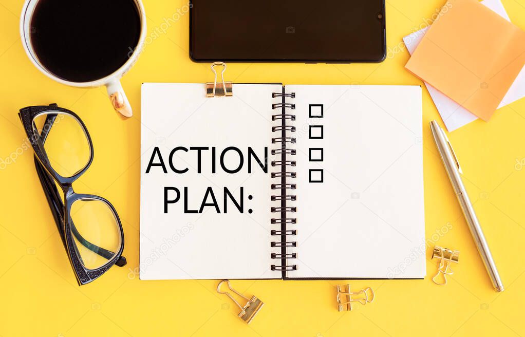 Notebook with action plan. Workplace with smartphone, glasses, coffee ,notebook with action plan and pen on yellow table