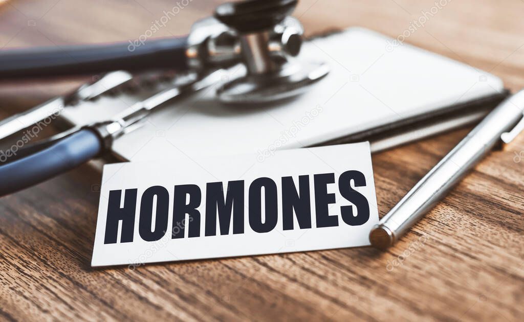 HORMONES word written on card on wooden table with medical background.
