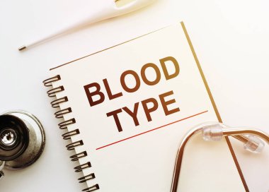 Tıbbi konsept. Beyaz masada stetoskop ve termometreyle birlikte KANLI TİPE yazan defter.