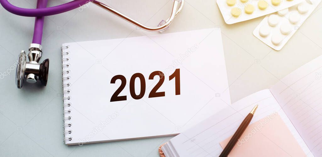 Stethoscope, pills and notebook with text 2021 on medical desk. 2021 medical vision