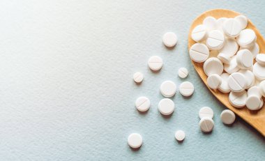 Beyaz haplar, mavi masadaki tahta kaşıkta tabletler. Tıp ve sağlık konsepti. Eczacılık. Üst Manzara. Haplar ve vitaminler.