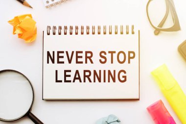 Asla Öğrenmeyi Durdurma, beyaz masadaki defterde el yazısı alıntısı, kalemler, büyüteç ve gözlüklerle